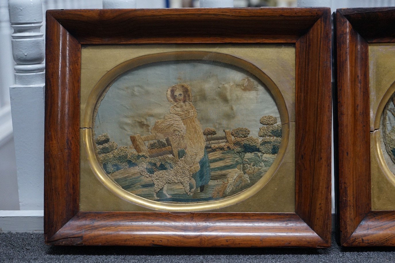 A pair of early 19th century rosewood-framed silk worked oval embroideries. Each embroidered with a boy and girl in a country landscape with their dogs. Worked in stem stitch and a knotting, the sky and faces hand painte